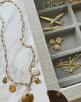Gold necklace with charms on a marble surface next to an open jewelry box with more gold jewelry pieces.