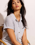 Woman wearing a light blue striped shirt sitting on a chair against a plain background