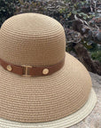 Beige straw hat with a brown band on a stone surface with greenery in the background