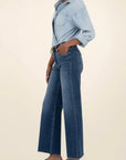Person wearing a light blue denim shirt and dark blue jeans on a beige background