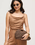 Woman in a brown outfit holding a matching clutch against a plain background