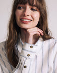 Woman wearing a white and gray striped shirt with a neutral background