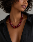 Woman wearing a red beaded necklace with a black shirt against a neutral background