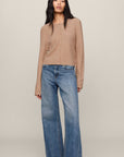 Woman wearing a beige sweater and blue jeans on a plain background