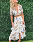 Woman in a floral dress standing against a green hedge