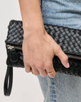 Person holding a black woven clutch bag with a plain background