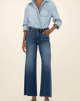 Person wearing a light blue denim shirt and dark blue jeans on a beige background