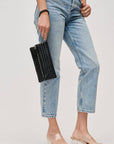 Person wearing light blue jeans holding a black clutch against a plain background