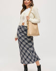 Woman wearing a plaid skirt, white top, beige cardigan, and black boots on a white background