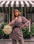 Woman in a checkered outfit holding a round woven bag in front of 'The Laundress' store.