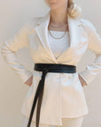 Person wearing a white blazer with a black belt against a plain background