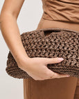 Person holding a brown woven clutch bag against a neutral background