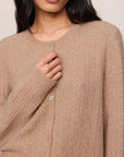 Close-up of a person wearing a beige cable knit sweater against a neutral background