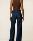 A model shown from the back wearing dark blue wide-leg jeans and a brown ribbed tank top, standing against a plain beige studio background.