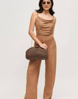 Woman in a brown jumpsuit holding a woven handbag against a plain background