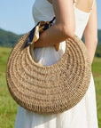 Person holding a woven bag in a scenic outdoor setting with greenery and mountains.