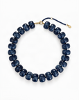A beaded necklace made of dark blue marbled beads, arranged in a circle on a white background. It features a gold-tone clasp and a navy blue beaded extender chain with a small gold tag.