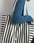 Person holding a black and white striped tote bag against a plain background