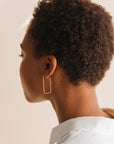 Person with short, curly hair wearing a gold hoop earring against a neutral background