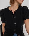 Person wearing a black cardigan with buttons on a plain background