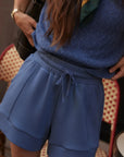 Person wearing a blue outfit with shorts and a sweater in an indoor setting.