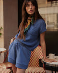 Woman in a blue outfit sitting at a cafe table with a cup of coffee.