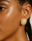 Close-up of a woman wearing a gold earring with a beige stone on a neutral background