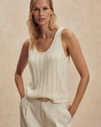 Woman wearing a white sleeveless top and beige pants against a beige background