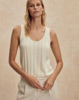 Woman wearing a white sleeveless top and pants against a beige background