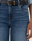 Person wearing blue jeans with a black belt and gold buckle on a neutral background