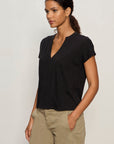 Woman wearing a black V-neck t-shirt and beige pants against a plain background