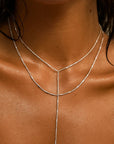 Close-up of a person wearing a thin silver necklace on a neutral background