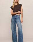Woman wearing a brown top and blue jeans against a beige background