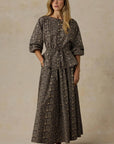 Woman wearing a long, patterned dress against a beige background