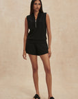 Woman wearing a black sleeveless top and shorts on a beige background