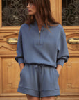 Woman wearing a blue tracksuit standing in front of a wooden door with intricate designs.