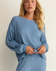 Woman wearing a blue ribbed sweater and pants against a plain background