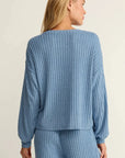 Woman wearing a blue ribbed sweater and pants on a beige background
