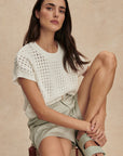 Woman sitting on a chair wearing a white lace top and light green shorts.
