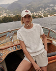 Woman on a boat wearing a white textured top and beige shorts with a scenic background.