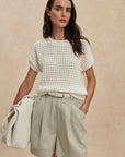 Woman wearing a white textured top and light green shorts against a beige background