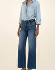 Person wearing a light blue denim shirt and dark blue jeans on a beige background
