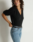 Woman wearing a black top and blue jeans against a plain background