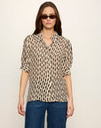 Woman wearing a patterned blouse and blue jeans against a plain background