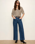 Woman wearing a patterned blouse and blue jeans against a white background