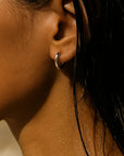 Close-up of a person's ear with a gold hoop earring, hair partially covering the face.