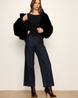 Woman wearing a black fur coat, black top, and dark jeans on a white background