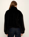 Person wearing a black fluffy jacket and dark jeans on a white background