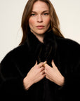 Woman wearing a black fur coat against a plain background