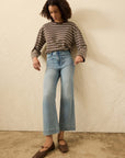 Woman wearing a striped sweater and blue jeans against a beige wall.